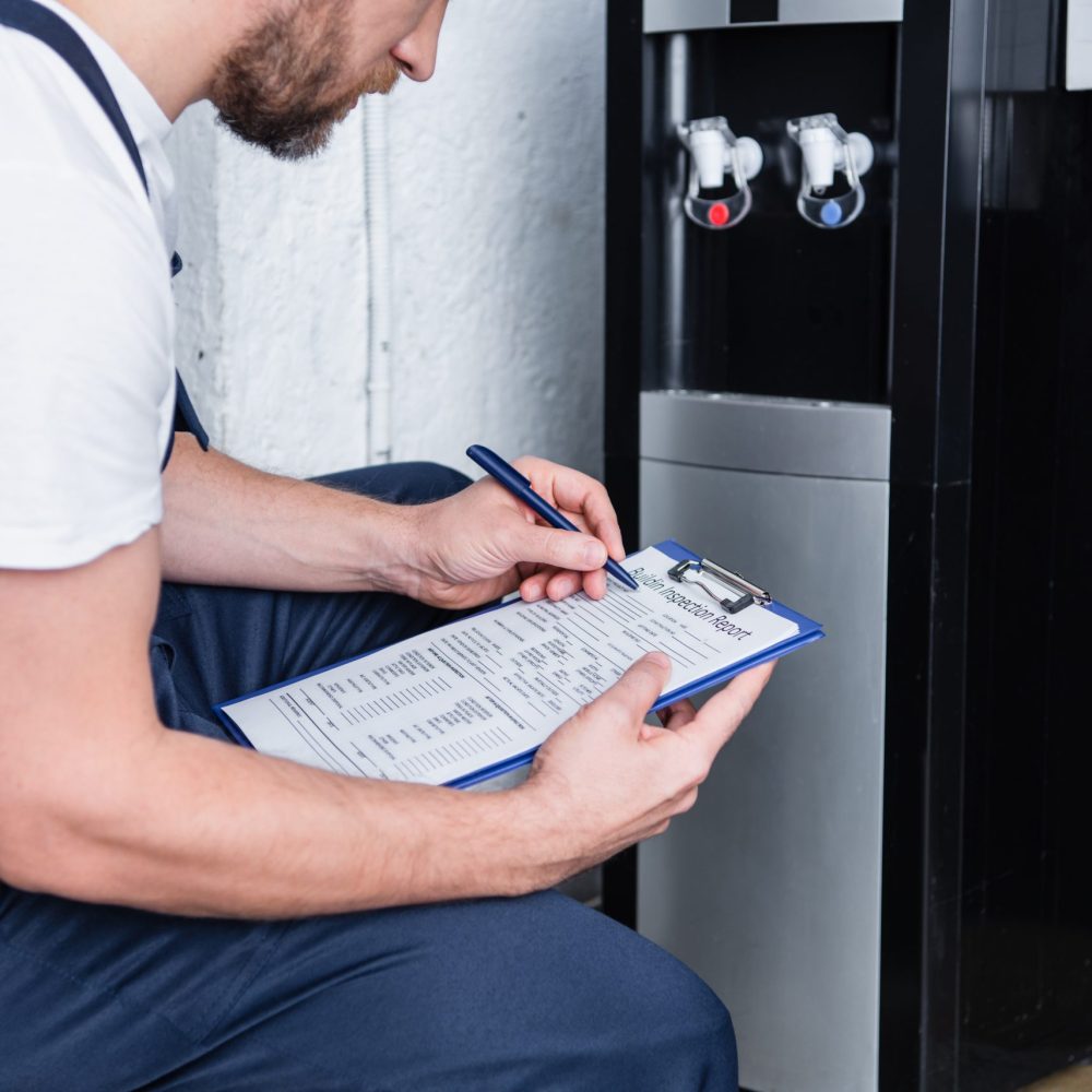 partial view of male repairman writing in clipboard during checking of broken water cooler