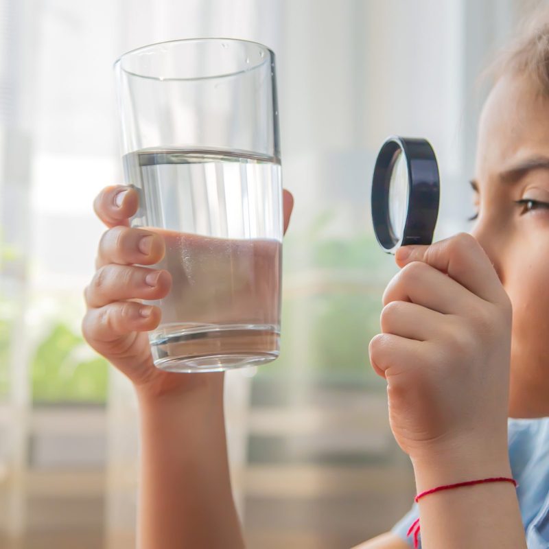 The child examines the water with a magnifying glass in a glass. Selective focus. Kid.